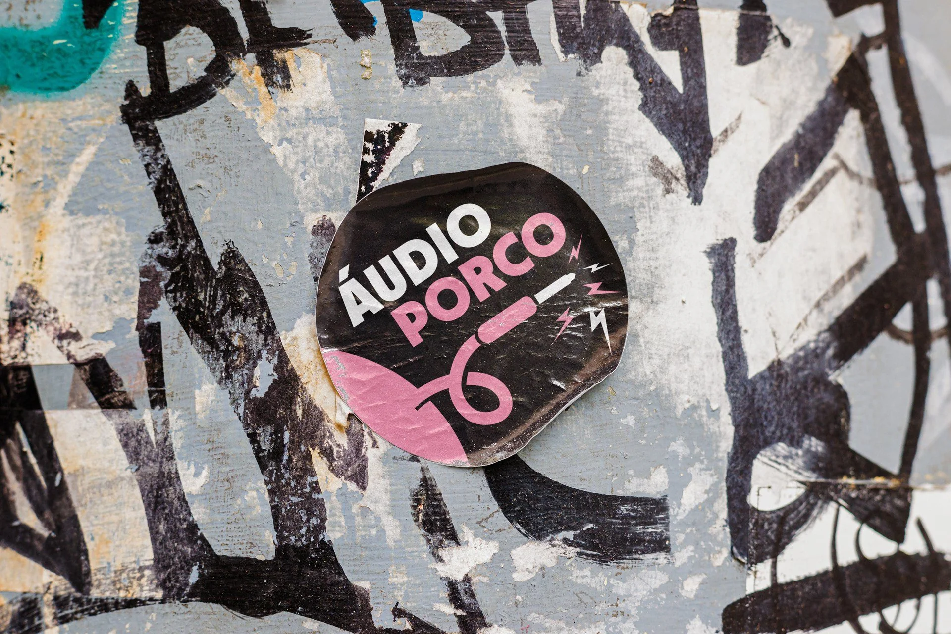 Round Áudio Porco sticker on a wall covered in tags