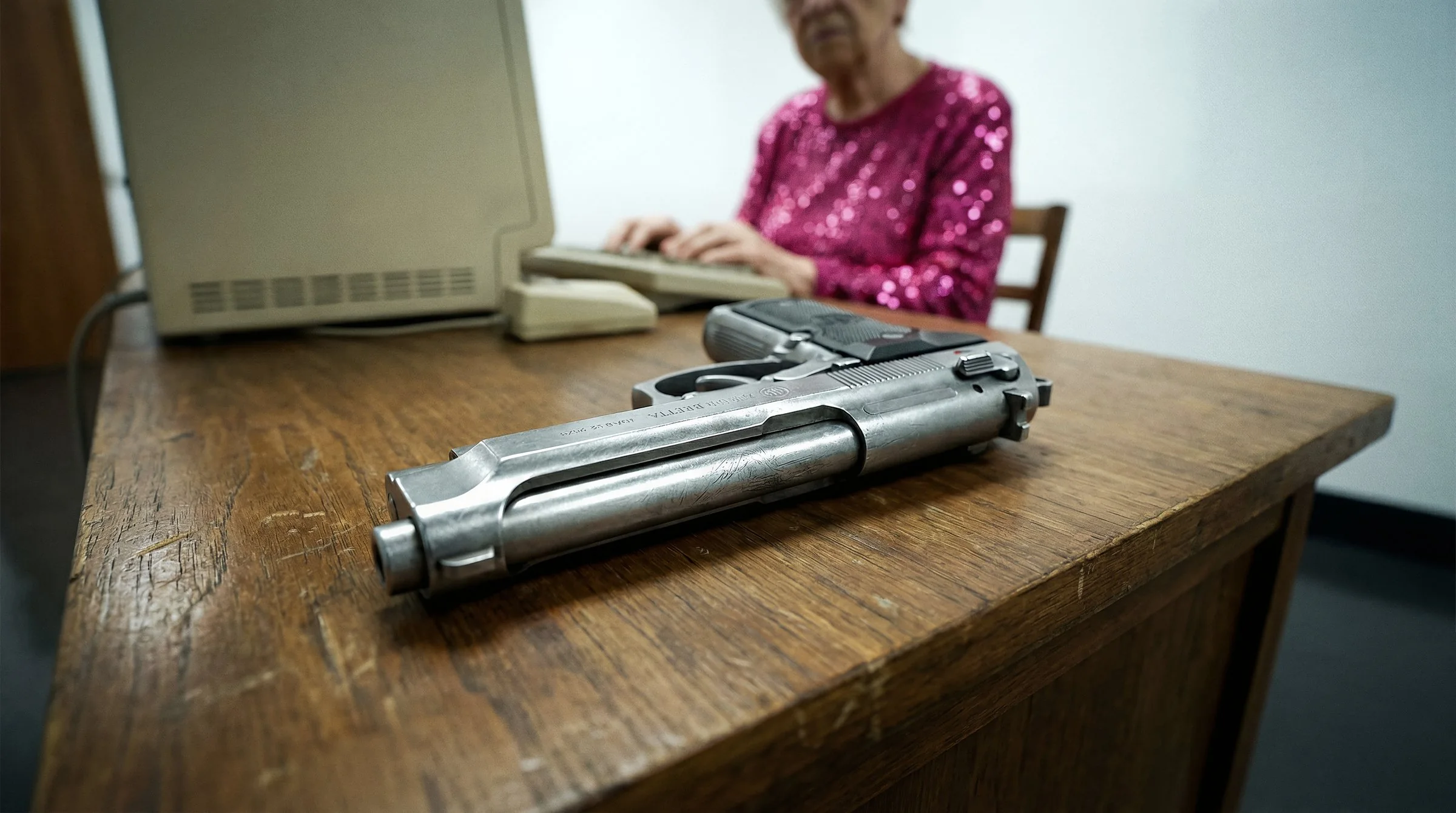 A pistol lies on the wooden desk in front of the examiner