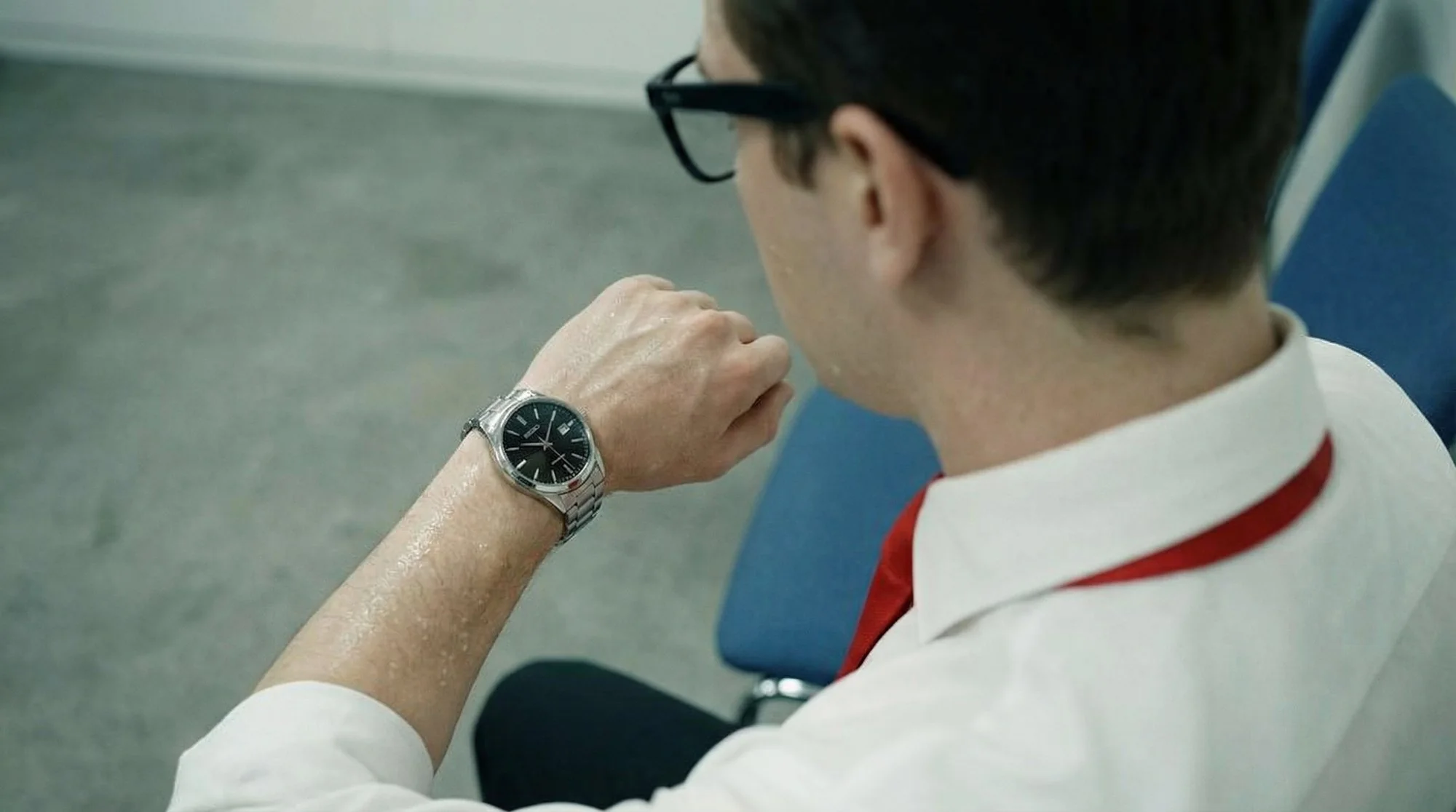 Elias checks his watch, his arm wet with sweat