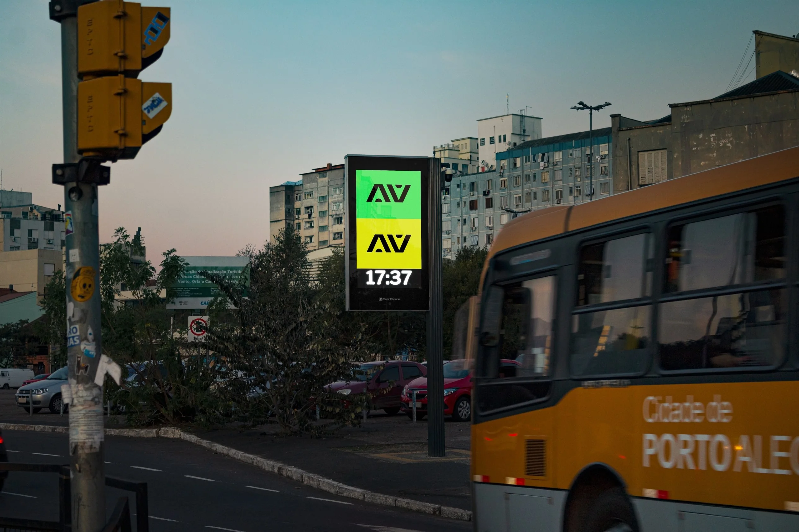 Digital street clock showing an animated AV piece at dusk, with a city bus passing