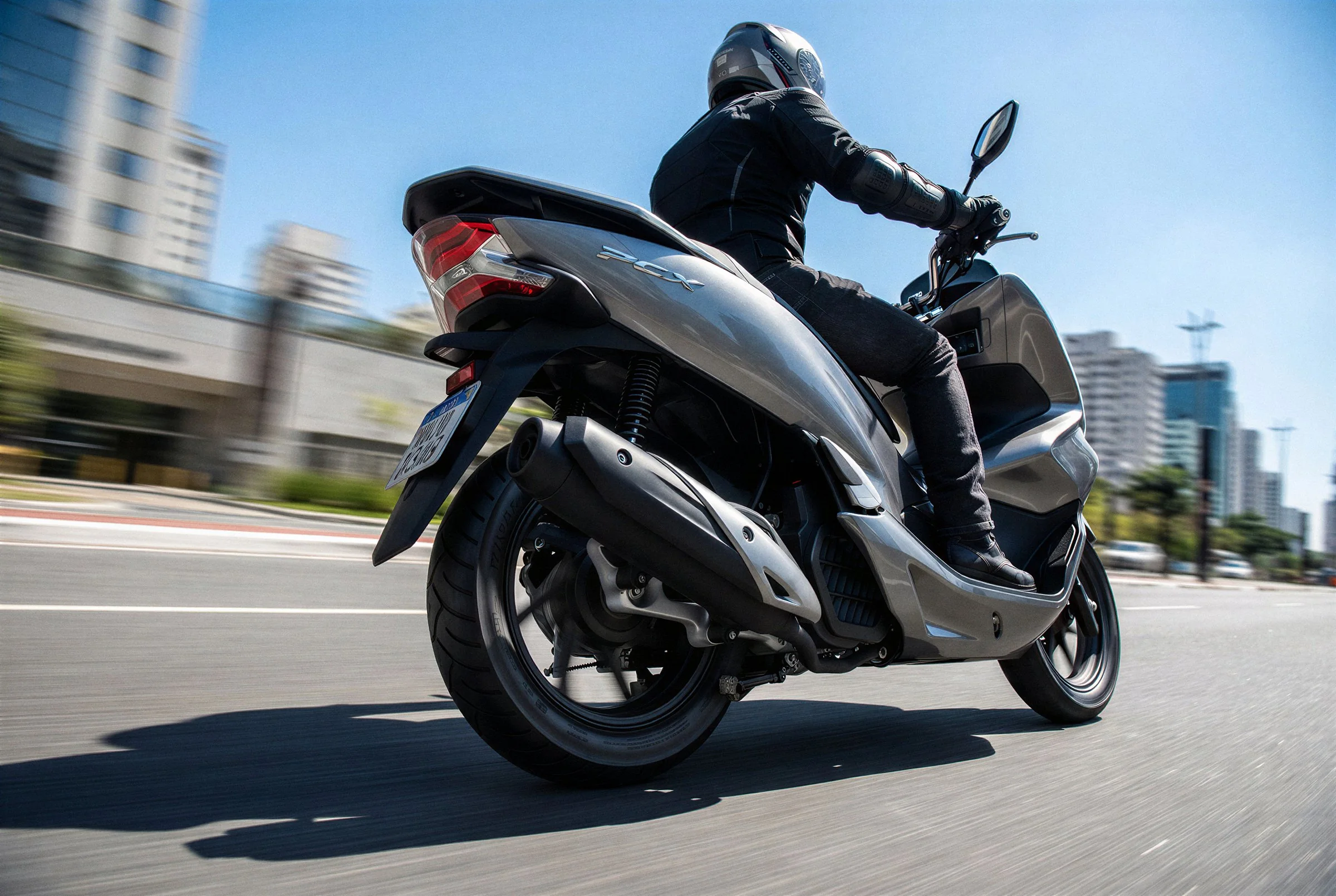 Honda PCX riding fast on a sunny city avenue