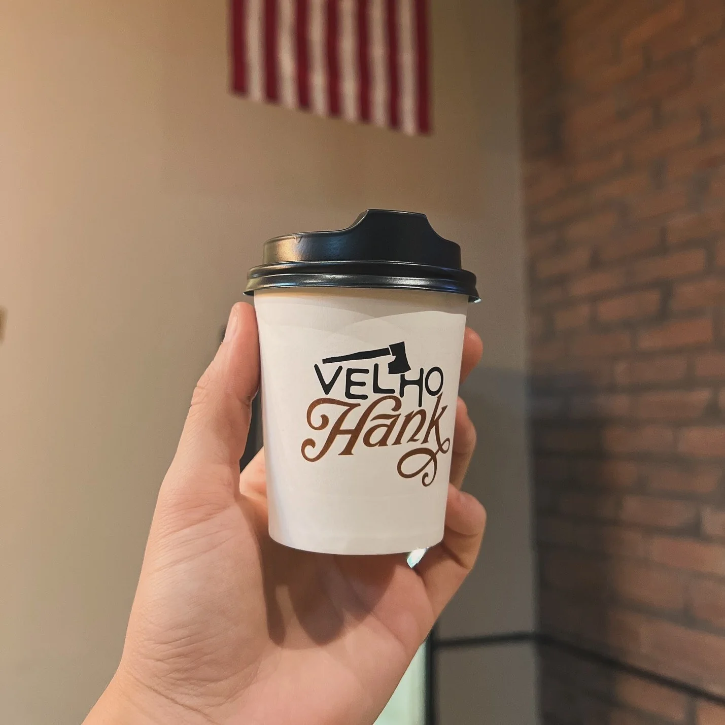 Hand holding a Velho Hank paper cup under an American flag